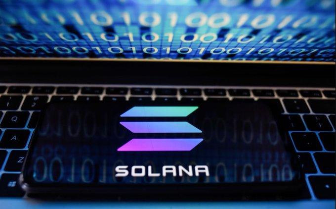 The Solana logo displayed on a smartphone screen against a laptop keyboard background with binary code.