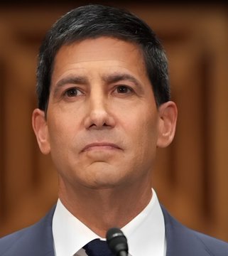 I can see a man with dark hair wearing a dark suit and tie, appearing to be in a formal setting that looks like a hearing or official proceeding with wooden paneling in the background. However, I'm not able to identify specific individuals based on their facial features.

As for the caption and connection to the post about US PPI data at 5.4%, I can describe the image and note that the post about Producer Price Index (PPI) data—showing inflation came in higher than expected at a two-month high—doesn't have a direct visual connection to this image of a man in a formal setting. If you could tell me who this person is, I could better describe how the image relates to the breaking PPI news.