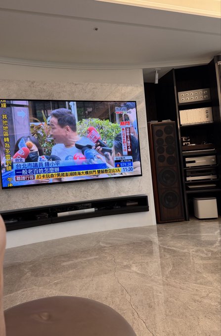 A young man in a blue Nike shirt watches intently at what appears to be a sports broadcast, with a news ticker visible showing financial gains ("up 84x"). The post humorously suggests the impressive investment returns shown on screen are too good to be true—likely "fake news."