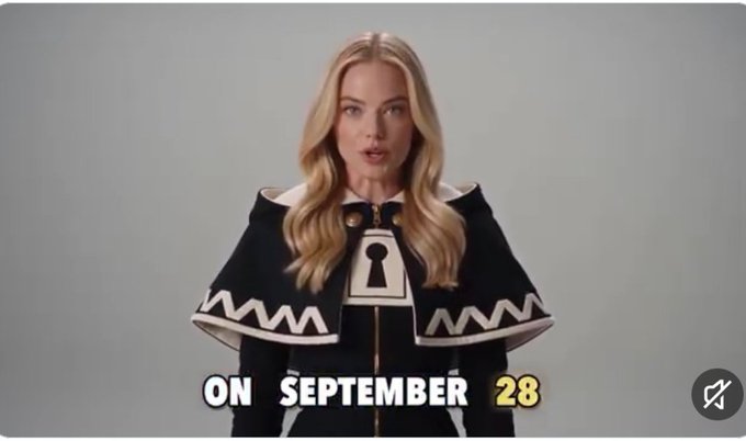 A blonde woman wearing a black cape with a keyhole design and white trim speaks to the camera, with text overlay reading 'ON SEPTEMBER 28'.