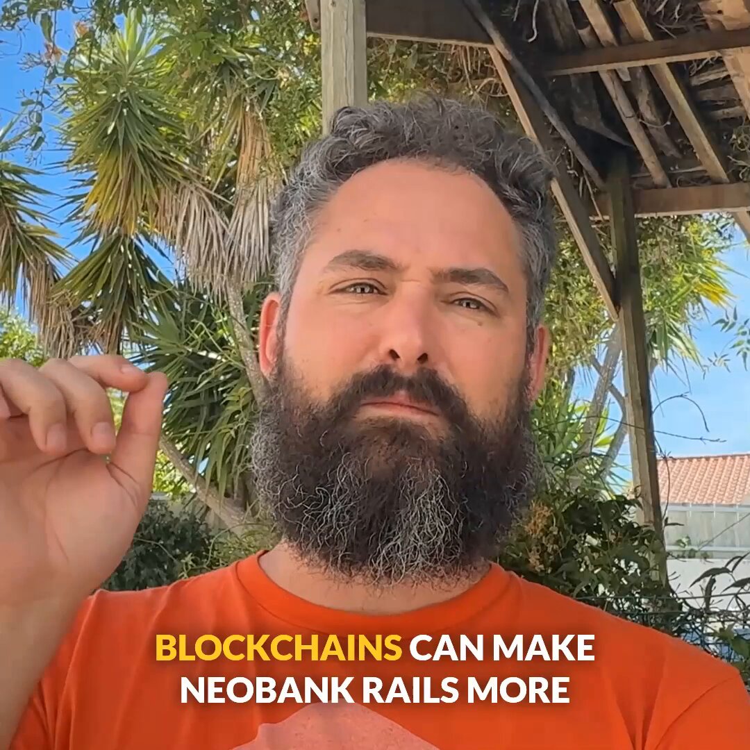 The image features a man with a beard wearing an orange shirt, standing under some trees. The background of the image shows a wooden structure or porch, which could be part of a house or another building. There are also palm trees visible in the scene. The main focus of the image is on the bearded man and his surroundings.