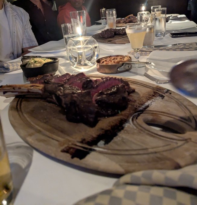 A rack of lamb and side dishes served on wooden boards at an upscale dinner gathering, with drinks and candles on the table—capturing the elegant dining experience shared by the Halifax crypto community hosted by Superteam Canada.