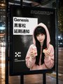 A woman stands beside a poster for the Genesis Hackathon, reading "GENESIS OKX黑客马拉松 AI交易所" alongside an "X3" logo, illustrating the team's participation in the #OKXAI hackathon event.