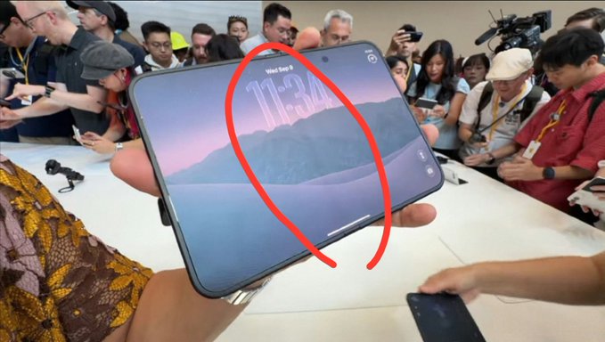 A folded smartphone is displayed in a crowd at what appears to be an Apple event, with a red circle highlighting the visible crease along the center of the screen showing the time "11:34" on Mon, Sep 9. The image illustrates the post's complaint about the persistent screen crease on the foldable device.