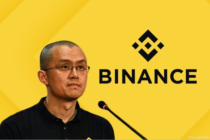 A man with glasses speaks into a microphone against a yellow background featuring the black 'BINANCE' logo and text.