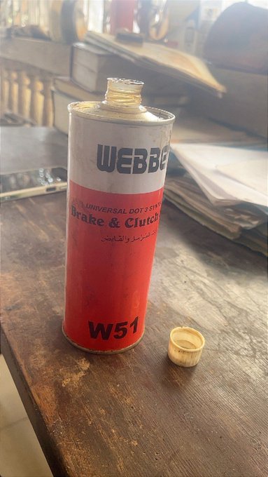 An empty can of "WEBBER W51" Universal DOT3 Brake & Clutch fluid sits on a wooden table with its cap removed, humorously paired with the caption "she left me guys" — a visual pun comparing the empty brake fluid container to a relationship drained of its substance.