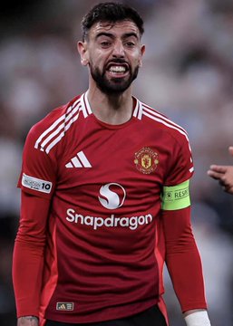 A Manchester United player, wearing the team's red home kit featuring the Snapdragon sponsor logo and a captain's armband, is captured with an intense expression during a match against Everton, which is the subject of the large $1.3 million wager placed on Polymarket for a United victory.
