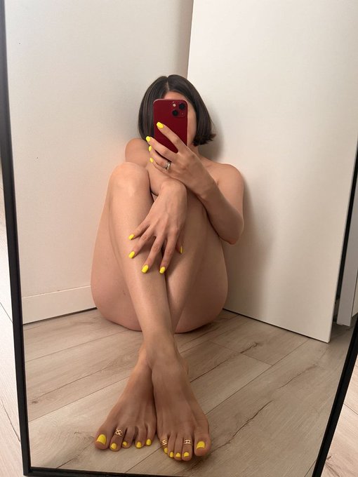 A person with a sleek black bob and bright yellow manicure/pedicure takes a mirror selfie while sitting curled up on the floor, their red phone covering their face.

The caption "she's the one" plays off the confident, minimalist aesthetic of the photo—the bold yellow nails against bare skin create a striking, unforgettable look that demands attention.