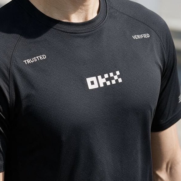A close-up photo shows a person wearing a black athletic t-shirt featuring the white logo 'OKX' on the chest, with the words 'TRUSTED' on the right and 'VERIFIED' on the left.