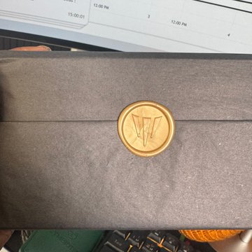 A gold wax seal embossed with a triangular logo on a black envelope, with a planner and keyboard visible in the background.