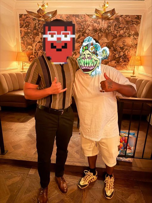 Two people stand in an ornately decorated room, one wearing a striped shirt and the other in a white t-shirt and shorts; both faces are obscured by digital overlays of a red pixelated character and a green goblin-like creature, and they are making hand gestures.