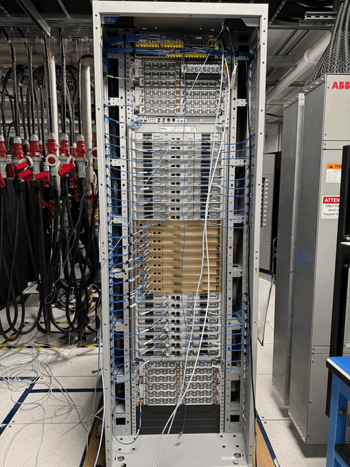 The image shows an industrial rack filled with numerous wires, likely used for data transmission or power distribution purposes. The rack appears to be in a factory setting, as there are several other racks visible in the background. A blue pipe can also be seen on one of the racks. The main focus of the image is the large rack that contains multiple wires and pipes, which may be part of an industrial machine or system.