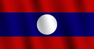 The image features a flag with red, blue, and white colors, which appears to be waving in the wind. The flag has a round center that stands out against the other colors. The background of the image is gray, providing a neutral backdrop for the vibrant flag. The caption "PI GCV News" suggests that this image might have been taken or published by Pi Global News, and it seems to be related to an article about Mr. Bounma Keopakdy's business in Laos.