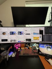 A desk setup with a curved monitor displaying various thumbnails, a smaller monitor above, and a colorful RGB keyboard and mouse.