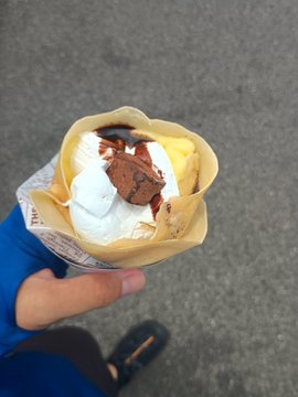 The image shows a person holding up an ice cream cone with chocolate, vanilla, and whipped cream toppings. The ice cream appears to be melting quickly due to its warm temperature. The photo also includes text that reads "#stepn近所のクレープ屋さんに10エナかけて たまにしかやってないので実は初めて買った アンカーとしておく". This text seems to be related to the ice cream cone, possibly indicating that it is a special edition or limited edition flavor.

The image also features a person's foot in the background, which could suggest that they are walking around while enjoying their ice cream treat.