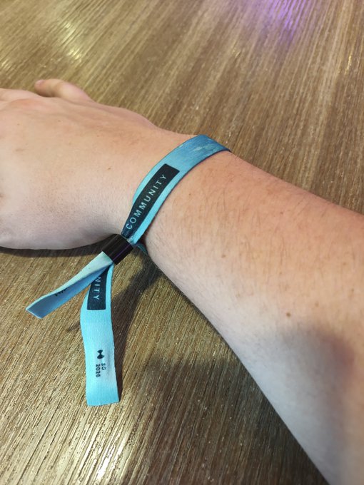 A person displays a light blue wristband on their wrist with "COMMUNITY" printed on it and "2024" along with "HYP" visible on the loose end, resting their arm on a wooden table. The image relates to the post as it shows the Hyperliquid festival wristband the user is trying to figure out how to remove.