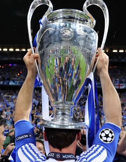 A player in a blue jersey lifts the UEFA Champions League trophy in a stadium filled with fans.