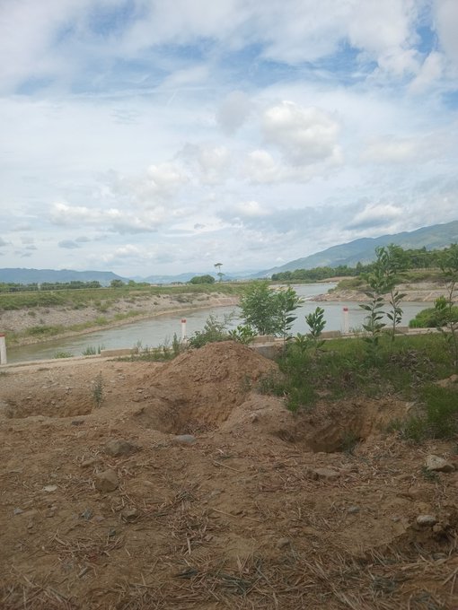 The image shows a large body of water surrounded by mountains, with a dirt road running through it. The sky above has some clouds, adding depth to the scene. There are also trees scattered around the area, providing a sense of scale and context for the viewer. The post in the image is titled "Chúc anh em ngày nghỉ cuần tuần vui vẻ nha Tầm này có usdt là vua hậu.", which translates to "The water in the middle of the mountains". The post is also titled "Chúc anh em ngày nghỉ cuần tuần vui vẻ nha Tầm này có usdt là vua hậu.", which translates to "The water in the middle of the mountains".