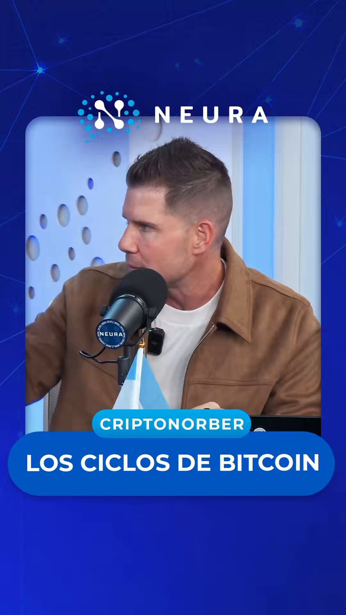 The image features a man wearing a brown jacket, speaking into a microphone while holding a microphone stand. The background of the image has blue text that reads "Los Cíclos De Bitcoin", which translates to "Bitcoin" in English. This suggests that the image is related to Bitcoin or cryptocurrency news and events.