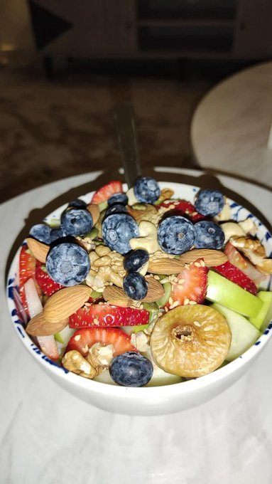 A bowl filled with a healthy mix of fresh fruits including blueberries, strawberries, figs, and almonds, with a spoon resting inside.