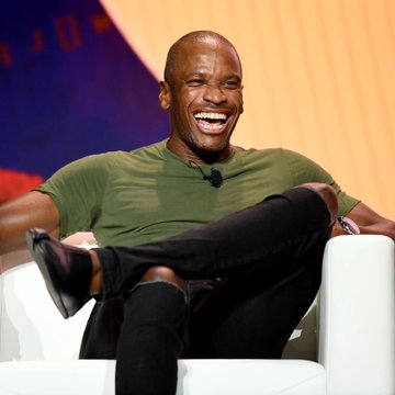 A man, resembling Arthur Hayes, laughs heartily while seated cross-legged in a white chair on a stage, wearing an olive green t-shirt. The image likely accompanies a post about Hayes' flipped yen thesis, suggesting his bullish outlook on Bitcoin amid potential Japanese market turmoil.