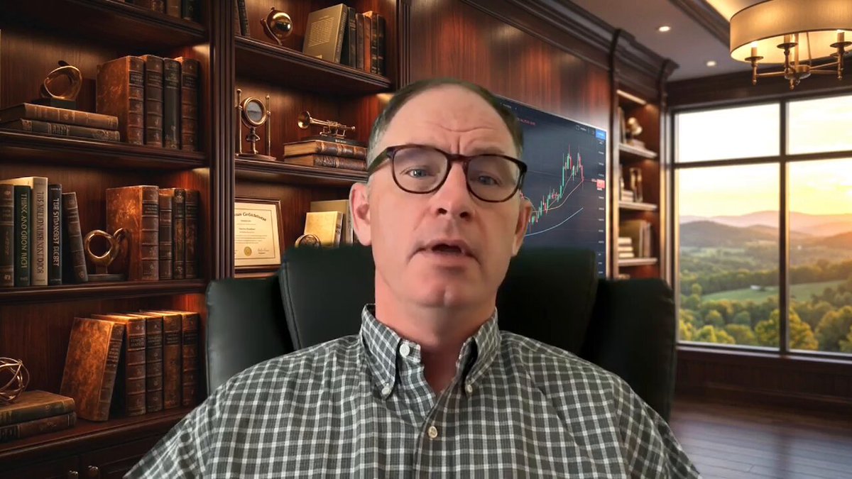 The image shows a man sitting in an office chair, wearing glasses and a plaid shirt. He appears to be giving a presentation or speaking into a camera. The background features a bookshelf filled with various books, suggesting that he might be discussing business or finance topics related to these books.