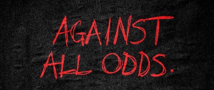 A motivational graphic with the words 'AGAINST ALL ODDS' written in red, handwritten-style text on a dark black chalkboard-like textured background.