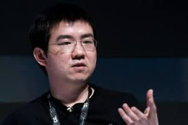 A man with glasses gestures while speaking at what appears to be a conference, likely discussing investment topics related to Bitcoin and AI as suggested by the accompanying post about $BTDR stock price predictions.