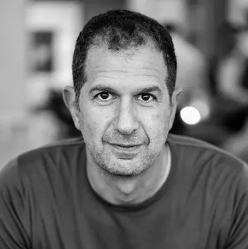 The image features a man wearing a gray shirt, sitting down with his head tilted back as if he's about to speak or make a statement. The photo has been edited to be black and white, giving it a timeless quality. In the background, there is another person partially visible, adding depth to the scene. The caption "Micky is cooking... $TIBBIR" suggests that the man in the image might be involved in some sort of culinary activity or event, possibly related to the post's title.

The photo has been edited with a grainy texture and a slight blur, giving it an artistic touch while maintaining its primary subject matter - the man wearing a gray shirt sitting down. The overall composition of the image is balanced, with the main focus on the man in the center of the frame against a blurred background that draws attention to him.