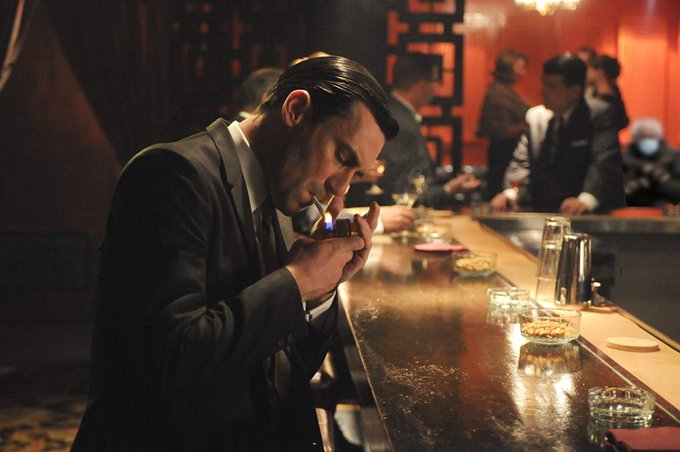 A man in a dark suit lights a cigarette at a dimly lit bar, with other patrons in suits visible in the background near what appears to be a "Hyperliquid" setting, possibly an event space or branded venue.

The dimly lit, cinematic atmosphere of the bar scene evokes the secretive, high-stakes energy often associated with decentralized crypto exchanges like Hyperliquid.