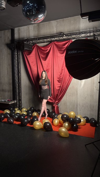 A woman poses in a dramatic photo studio setup featuring a red satin backdrop, disco ball, and black-and-gold balloon display on a red carpet, with a "Godox" lighting umbrella visible to the right—capturing one of the two photoshoots mentioned in her June recap.