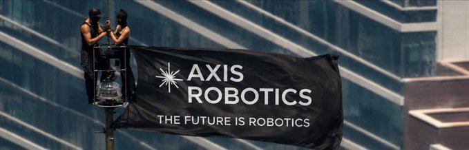 Two people in a bucket truck install a large black banner on a city building that reads 'AXIS ROBOTICS - THE FUTURE IS ROBOTICS' with a star-like logo.