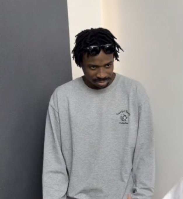 A man with dreadlocks and sunglasses perched on his head wears a gray sweatshirt and looks directly at the camera.