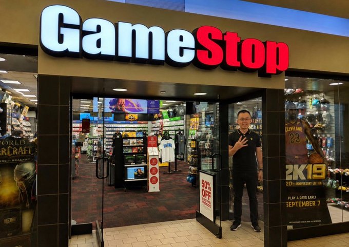 Exterior view of a GameStop store with the iconic logo sign above the entrance and NBA 2K19 promotional posters displayed on the windows.