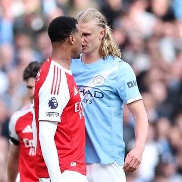 Two Premier League soccer players confront each other during a match, with one wearing a red and white Arsenal jersey and the other in a light blue Manchester City kit with 'ETIHAD AIRWAYS' sponsor text.