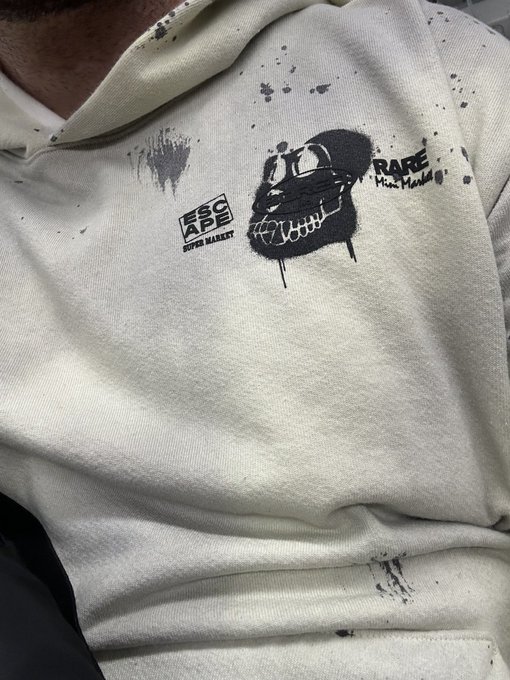 A close-up of a cream-colored Escape Market hoodie with a black spray-paint style graphic of a distorted smiley face with stitches and the text 'RARE' and 'Stussy Market'.