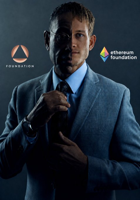 A man in a gray suit and blue shirt with glasses adjusting his tie, flanked by the 'FOUNDATION' logo on the left and the 'ethereum foundation' logo on the right.