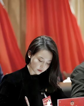A photo captures a woman with long dark hair looking down, with a red flag visible in the blurred background.