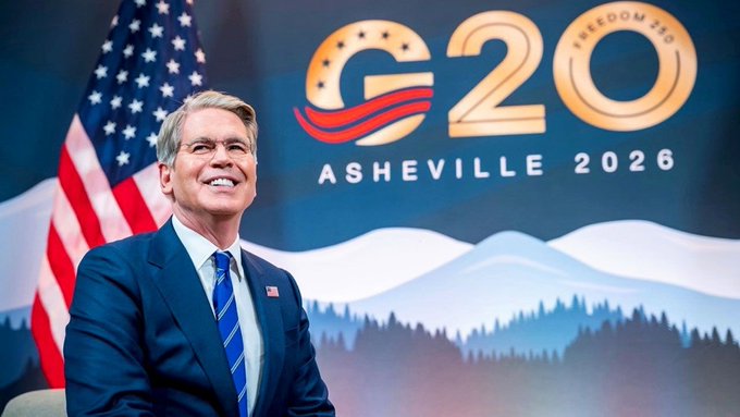 A smiling official wearing a blue suit stands in front of an American flag and a backdrop reading "G20 ASHEVILLE 2026," aligning with the post's announcement that G20 finance ministers and central bank governors recognized digital assets' role in economic growth and innovation while committing to responsible regulatory frameworks.
