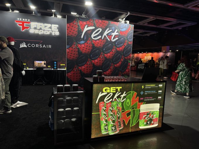 An expo booth features FaZe Esports and Corsair branding, with a colorful 'rekt' energy drink display in the foreground and attendees walking around the venue.