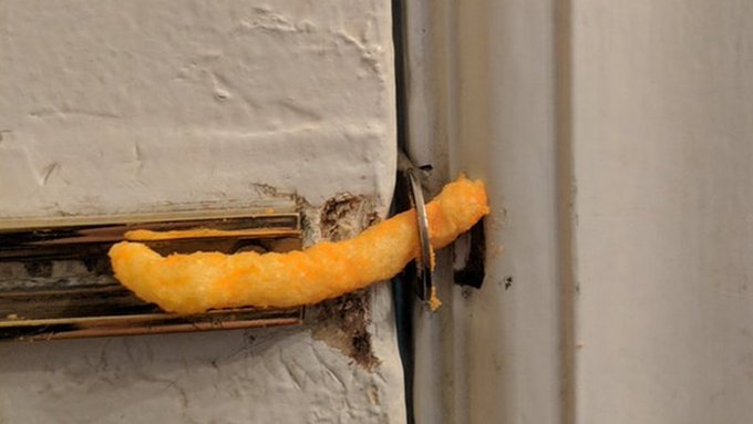 The image displays a close-up view of a piece of bright yellow cheese puffs, resembling a crumb, sticking out of an open door lock or a metal door handle. The perspective creates an artistic and unusual composition that combines elements from everyday life with the unconventional use of food as an object for artistic expression. In the context of the post, it seems to be promoting a negative viewpoint on the current state of political leadership in America through the unusual juxtaposition of cheese puffs and a mundane household object like a door handle or lock. The image's message could be seen as a reflection of dissatisfaction with the current situation, suggesting that the political system may not be functioning optimally for the majority of citizens, just as the cheese puffs are not being used appropriately in their intended context.