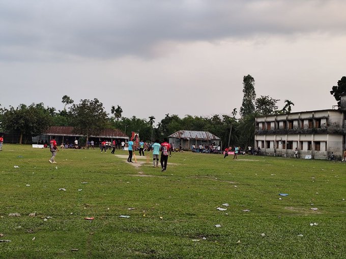 The image shows a group of people playing soccer on a field, with some players standing near each other while others are scattered across the field. There are also several individuals sitting or standing around the edges of the field. In the background, there is an old building and trees, adding to the overall atmosphere of the scene. The post contains text that reads "Good morning X Fam. Can I get a Gm? Do you guys support sports @NomismaNetwork @useTria Quacks @TheARCTERMINAL". This suggests that the image might have been taken during an event or gathering related to soccer, and the people in the photo are likely participants or spectators of this event.