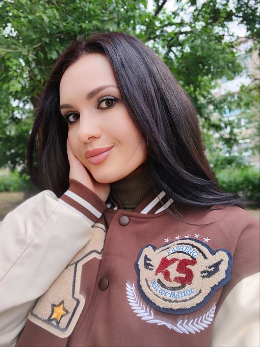 A woman with long dark hair posing outdoors, wearing a brown and cream letterman-style jacket with a "Casablanca" patch and the number "75".