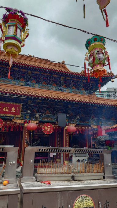 A traditional Chinese temple with ornate decorations, red lanterns, hanging flower lanterns, and an incense altar in the foreground with burning incense sticks.