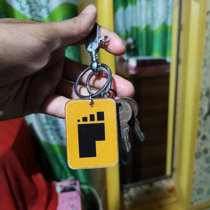 A hand holds a keychain with a yellow tag displaying a black "P" logo, attached to two metal keys.