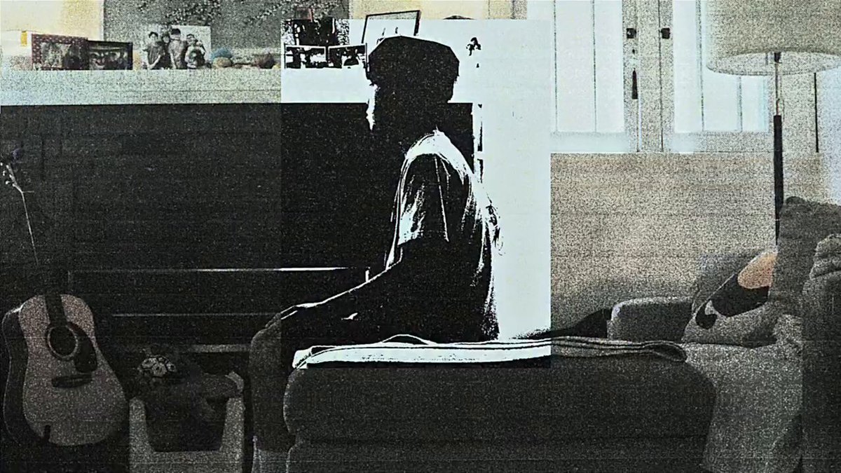 The image shows a person sitting on a couch, possibly watching TV or playing an instrument like a guitar. The scene takes place in a living room with a fireplace nearby. There are two other people present in the room as well, one of them holding a guitar and another person sitting on a chair. A lamp is also visible in the background. The image has been shared on social media, where it has received numerous likes and comments from various users who appreciate its artistic composition and the way it captures everyday life moments.