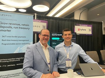 Two representatives from iFinex/Cosmos stand at their FinovateFall booth, with marketing text promoting "Grow revenue, retain deposits, run treasury smarter" and features like "24/7 cross-border payments" and "Real-time treasury management" displayed on banners behind them.