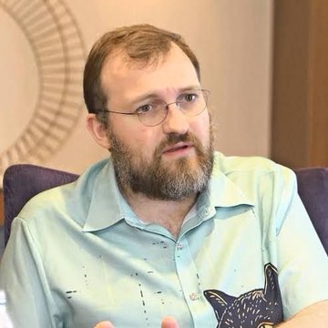 A bearded man with glasses wearing a light blue patterned shirt speaks during what appears to be a panel discussion or interview, likely representing the Cardano ($ADA) ecosystem in connection with the announcement of programmable tokens going live on Cardano's mainnet. The setting suggests a conference or professional event related to blockchain technology and tokenization developments.
