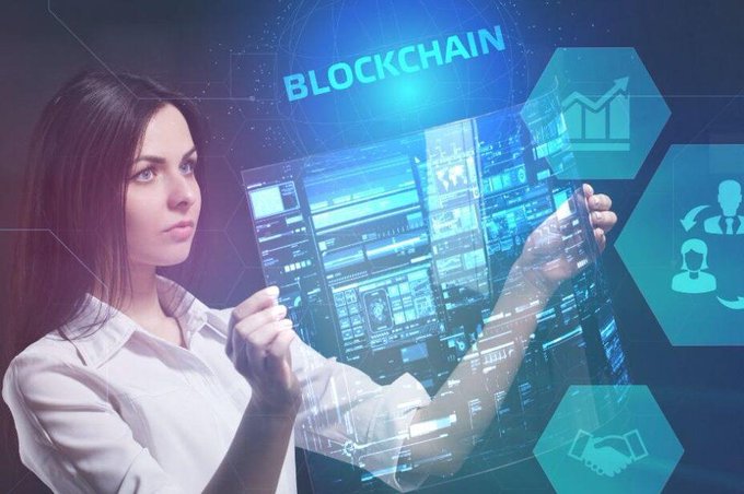 The image features a woman wearing a white shirt who appears to be using her phone or tablet with an AI interface displayed on its screen, possibly interacting with a virtual assistant or a chatbot. The background of the image has various icons related to technology and business, such as a computer monitor, a keyboard, and a mouse. The caption above the image reads: "AI is lowering the cost of creation. The real question is: who owns what gets built?". This suggests that AI is playing an increasingly important role in the development and creation of new applications or services, potentially impacting various aspects of our lives, including business and technology.