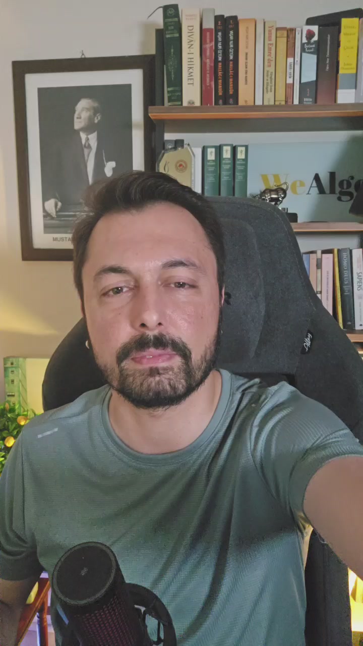 The image features a man sitting in front of a bookshelf filled with various books. He has a microphone in his hand, which could be used for recording podcasts or live streams related to cryptocurrency, gold, oil, or other financial topics. The background includes a picture and a clock on the wall, suggesting that he might be working from home or attending an online event.